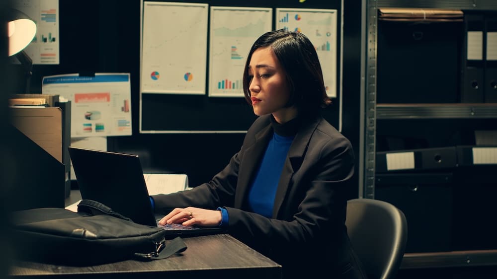 Woman working on laptop in dim office.