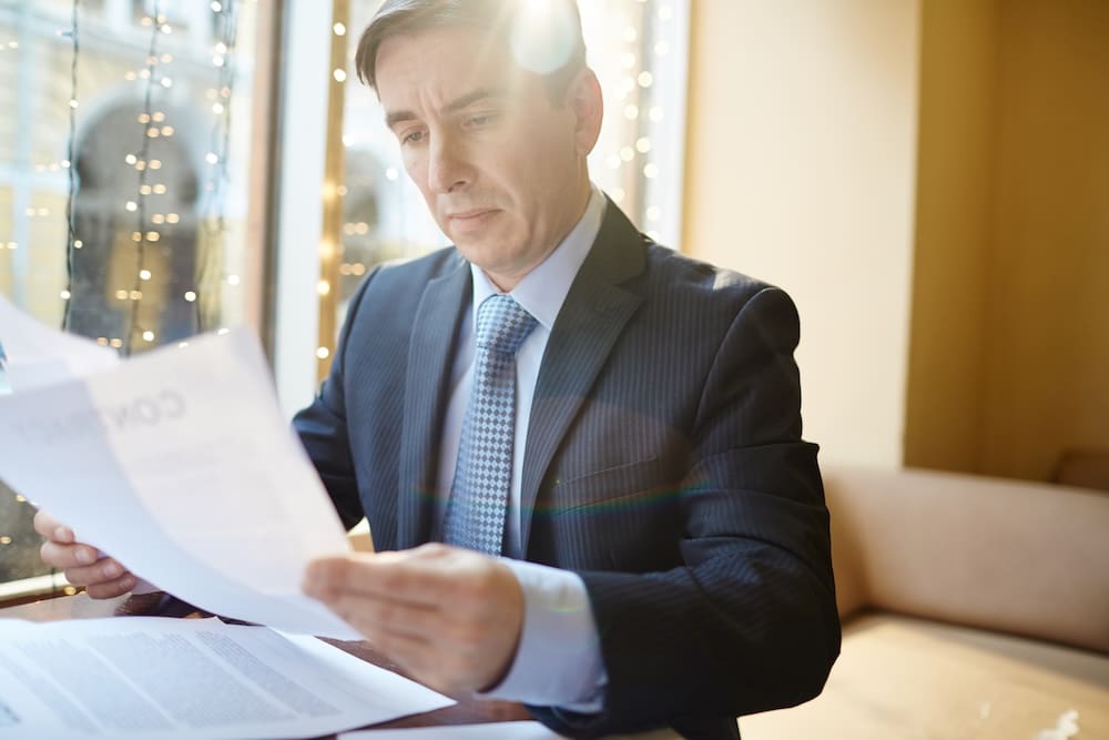 Man in suit reading documents by window.
