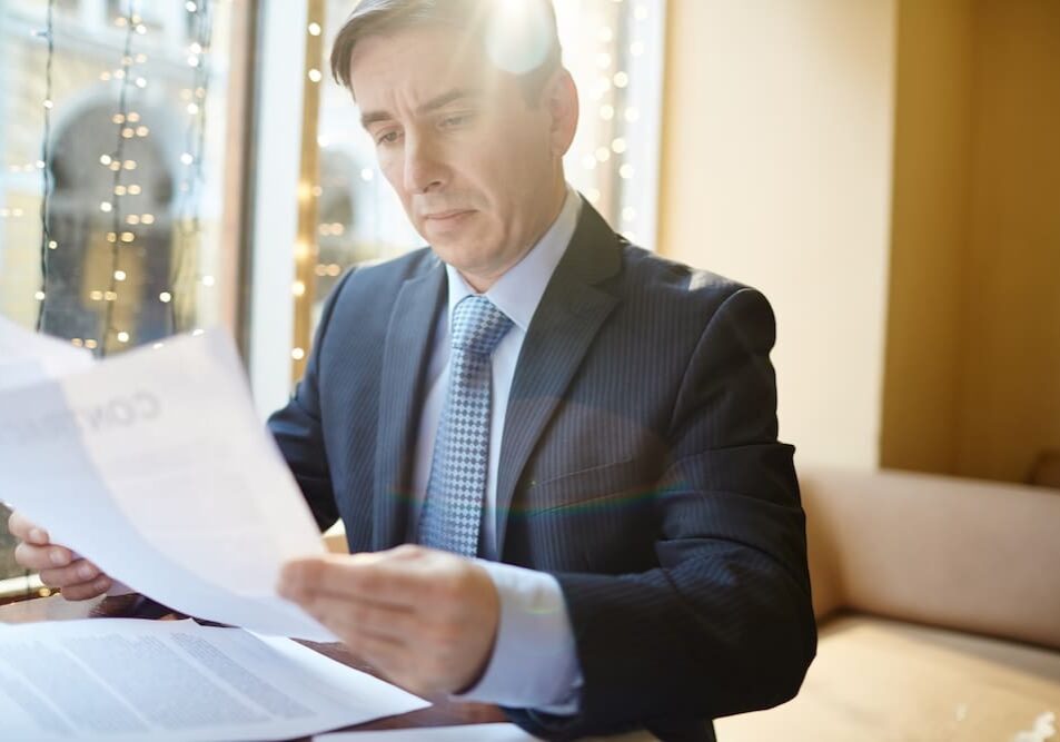 Man in suit reading documents by window.