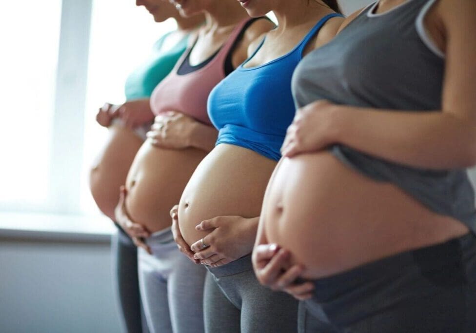 Pregnant women standing in a row indoors.